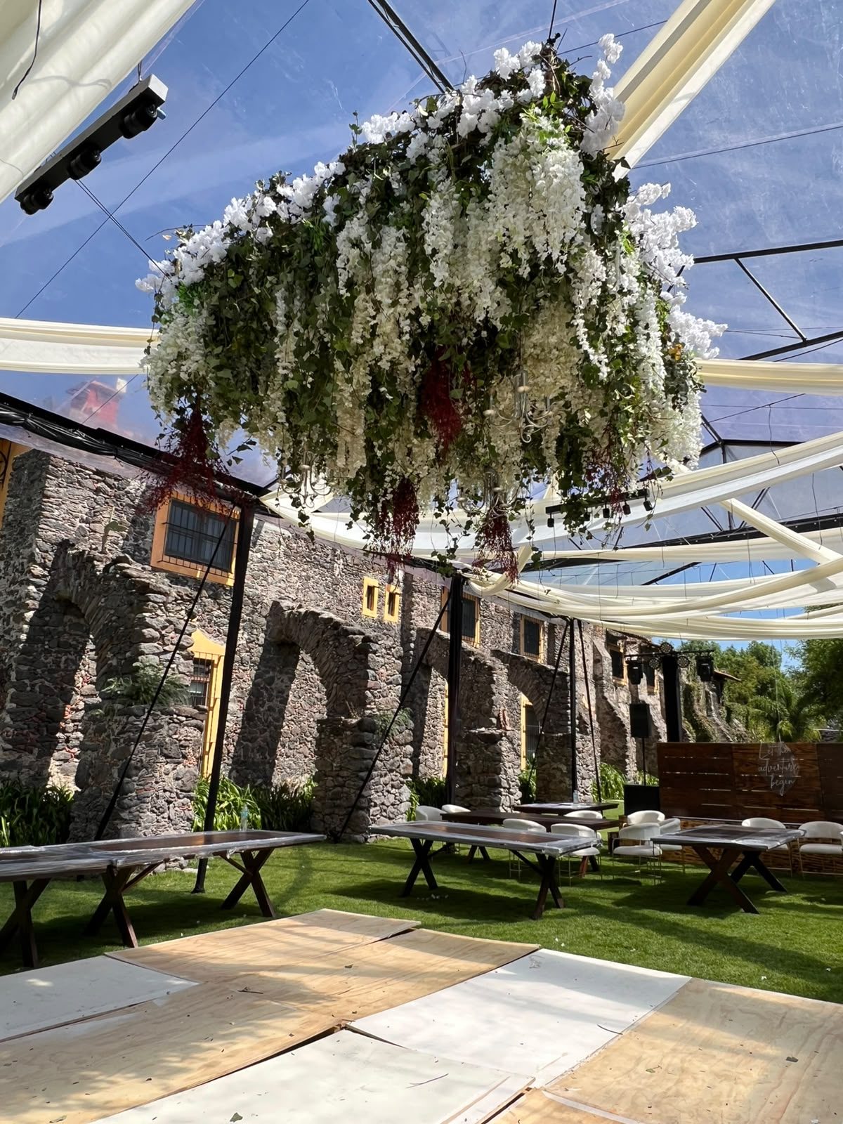 Pista de baile con instalación floral colgante bajo carpa transparente para boda en Hacienda Dolores, Querétaro